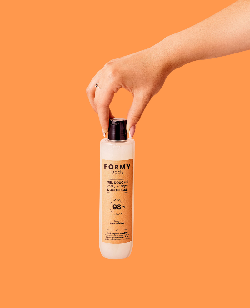 Une main de femme qui tient mon gel douche Zesty Energy