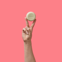 Une main tient mon shampoing solide cheveux colorés et méchés entre ses doigts