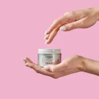 Une main tient le pot de ma crème jour et une autre main va vers l'intérieur du pot