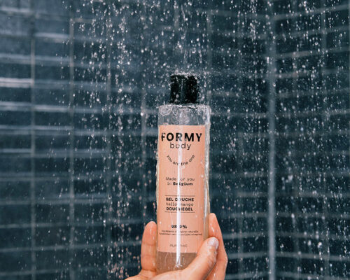 Main tenant verticalement un flacon de gel douche Hello Mango sous la douche qui coule
