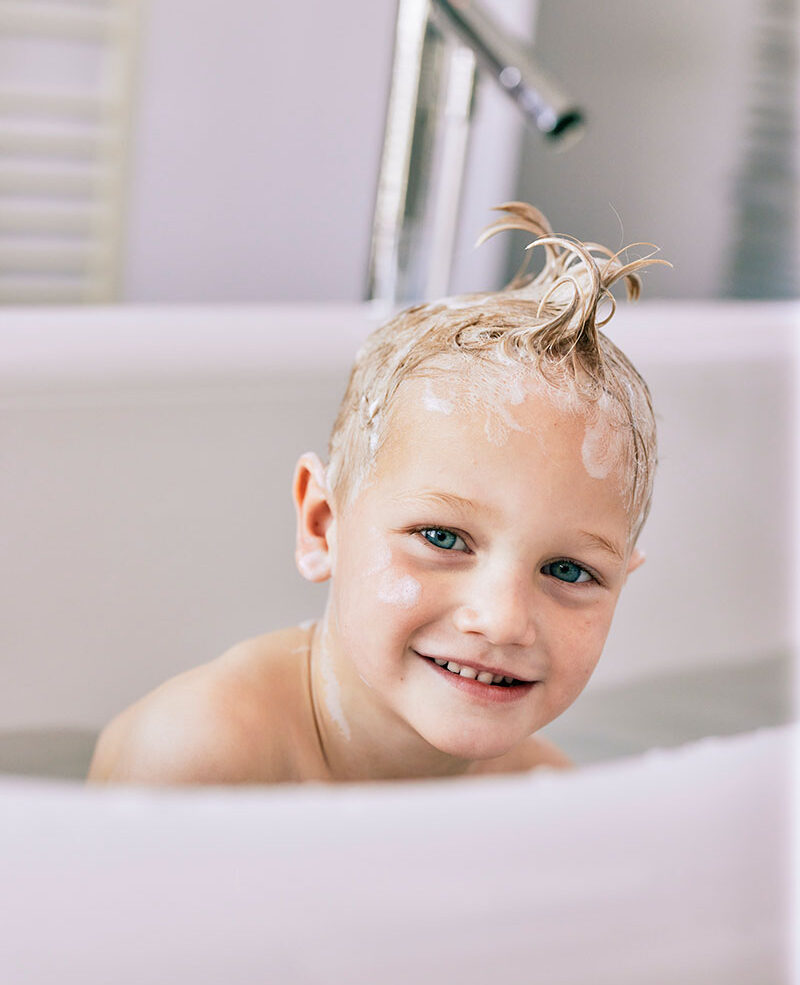 Formy shampoing solide Tête d'une enfant souriant accroupi dans son bain avec du shampoing solide et de la mousse dans ses cheveux