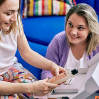 Deux femmes assises, l'une d'entre elle tient un gel douche Hello Mango devant un coffret cadeau ouvert.