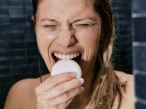 Femme de face croquant et souriant dans un shampoing solide sous la douche