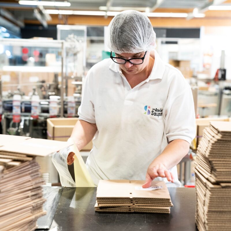 Femme avec une charlotte sur sa tête pliant des cartons au Saupont