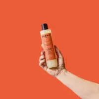 Une main tient mon flacon de shampoing liquide cheveux secs et abimés