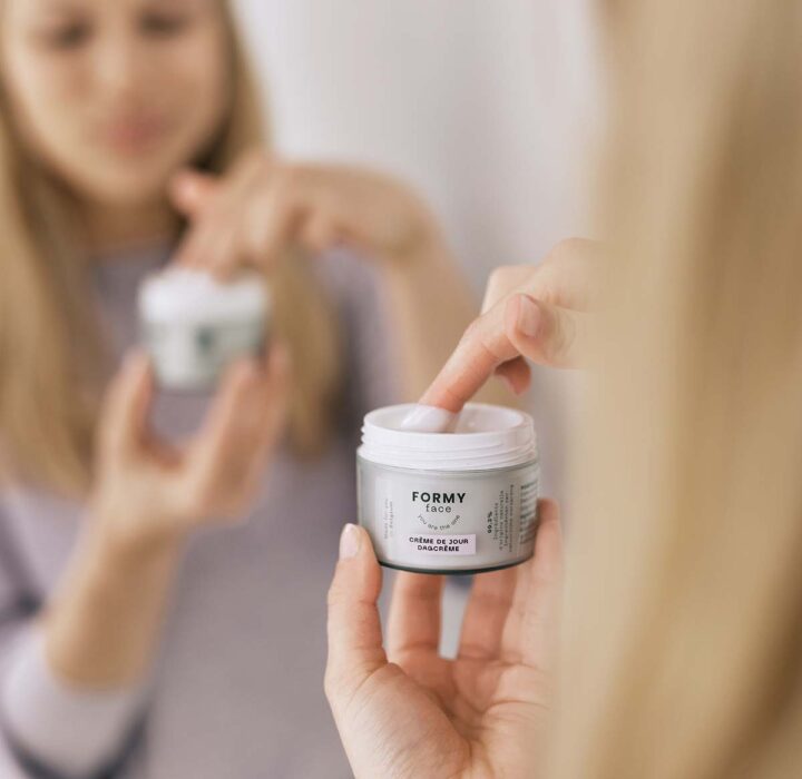Une femme met sa main dans le pot de ma crème visage jour